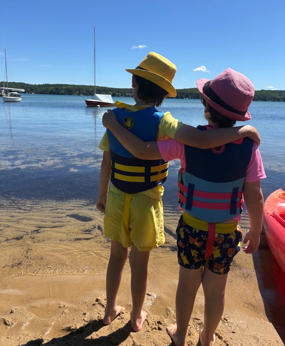 Two kids looking out at the lake wearing hats.